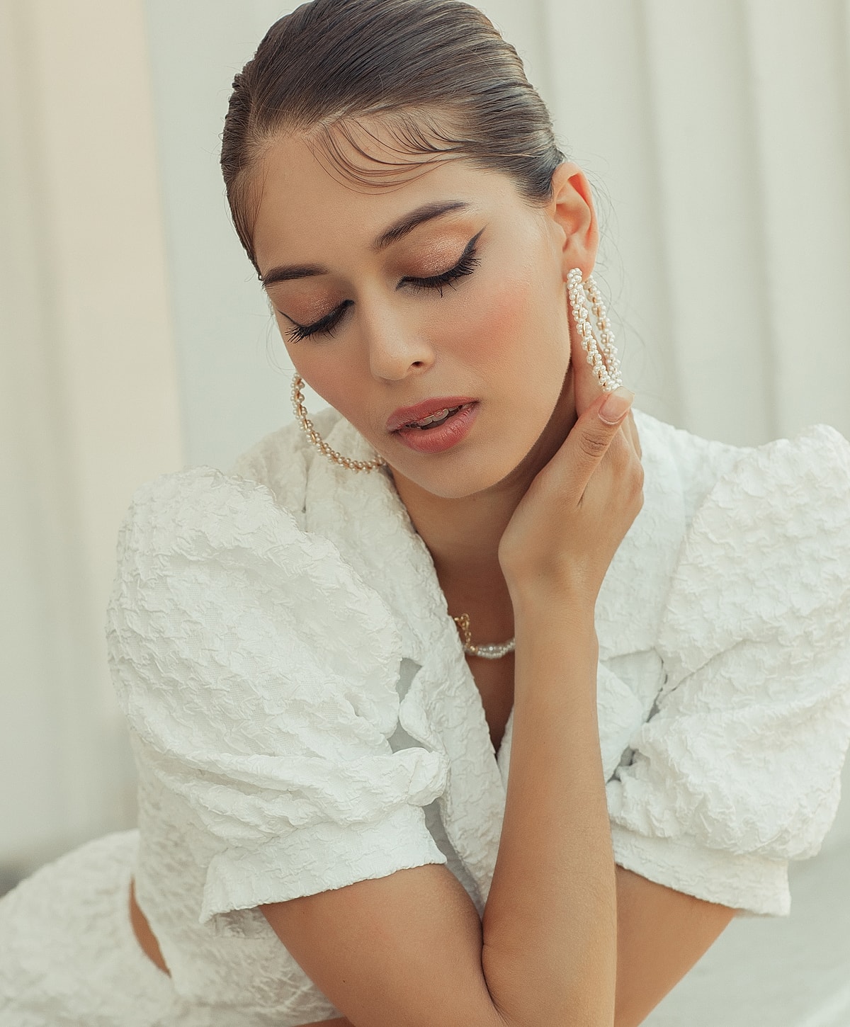 Woman in white outfit with elegant hairstyle and earrings.