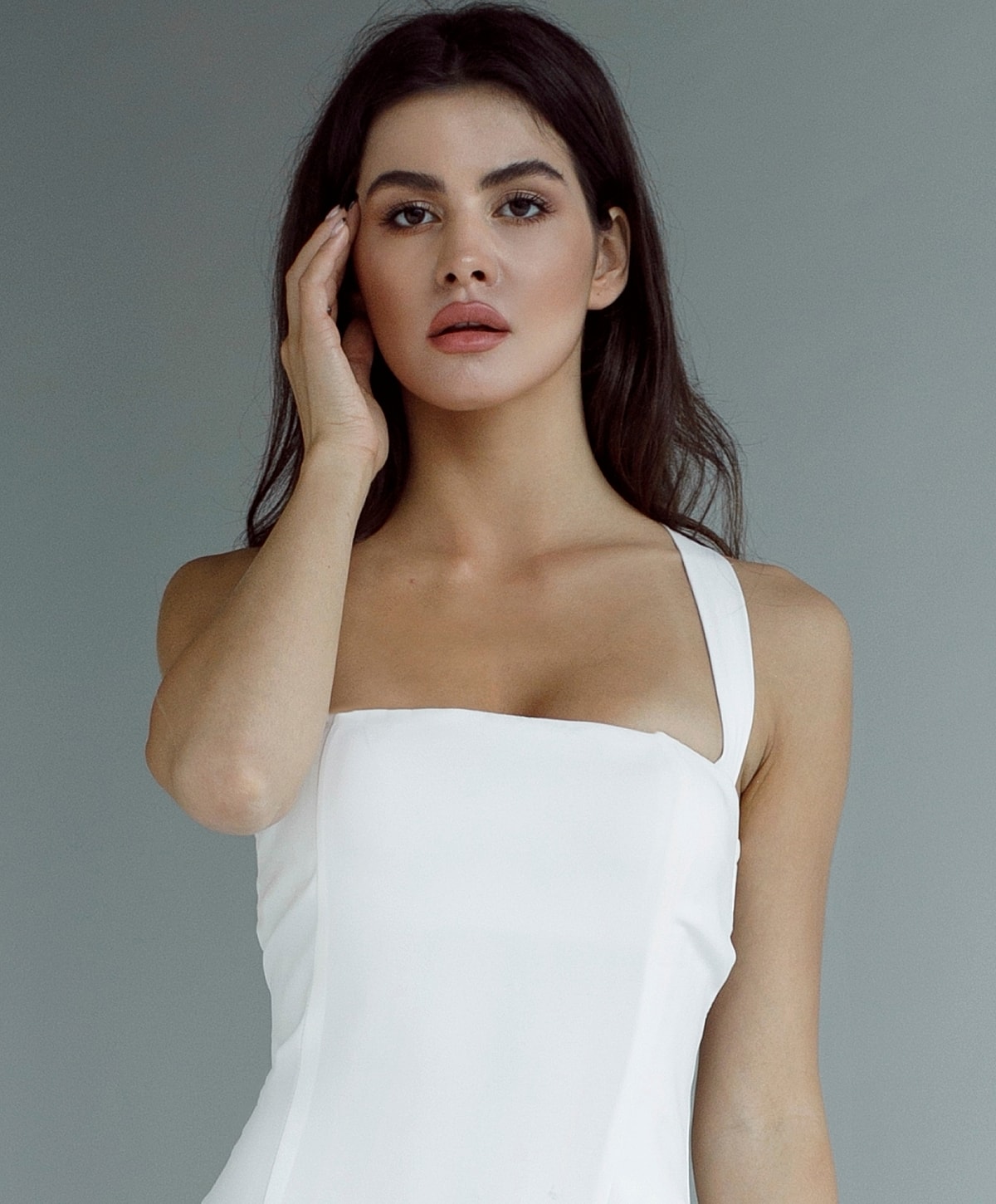 Woman in white dress posing against gray background.