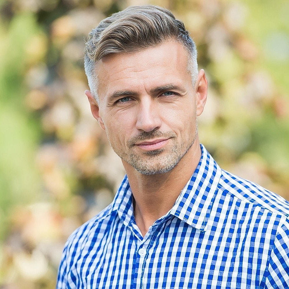 Man in checkered shirt smiling outdoors.