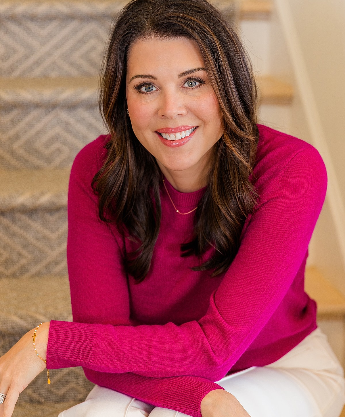 Smiling woman sitting on stairs, wearing pink sweater.