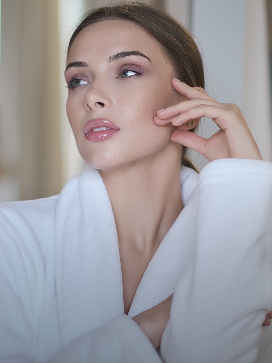 Woman in white robe posing thoughtfully indoors.