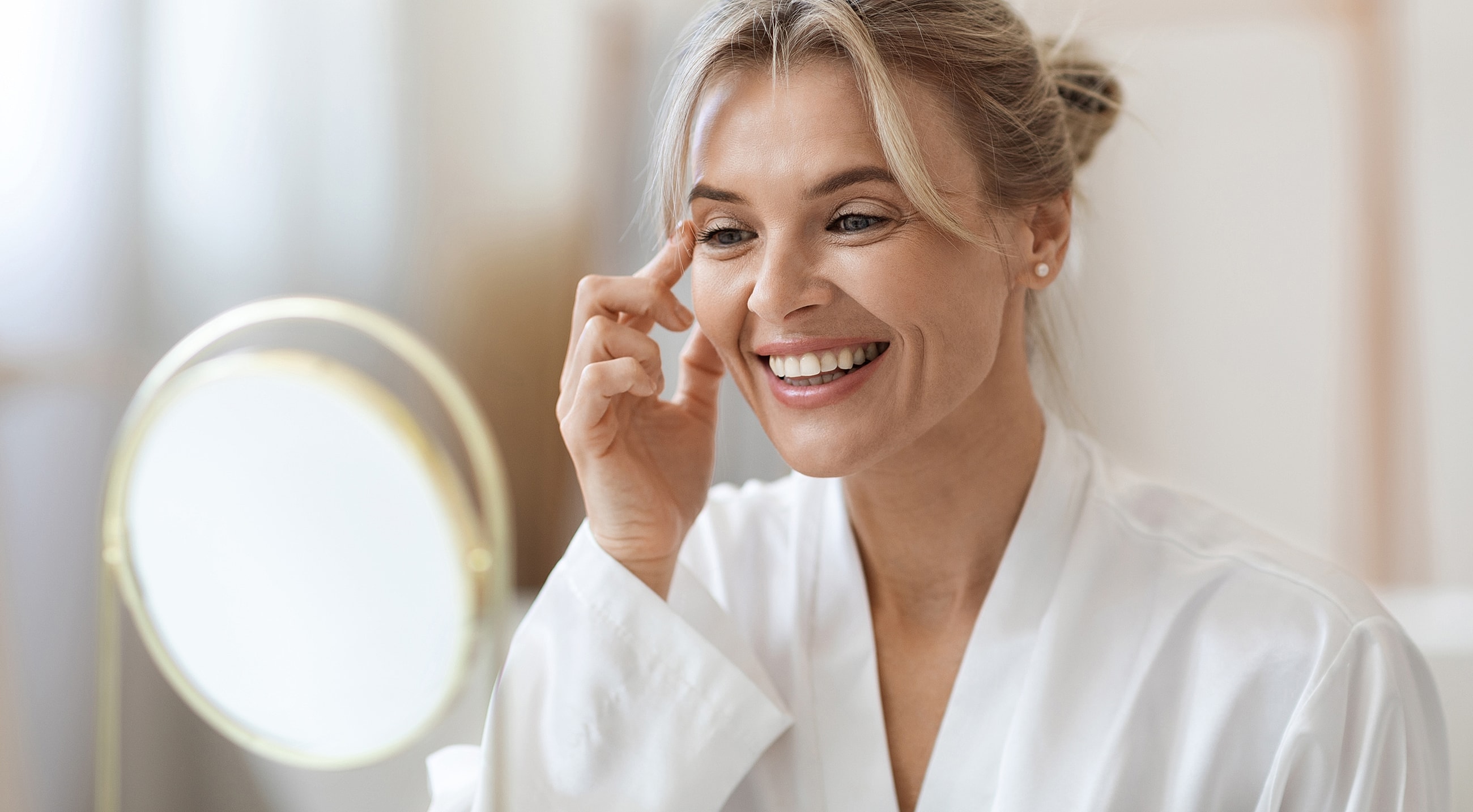 Woman applying skincare while smiling in mirror.