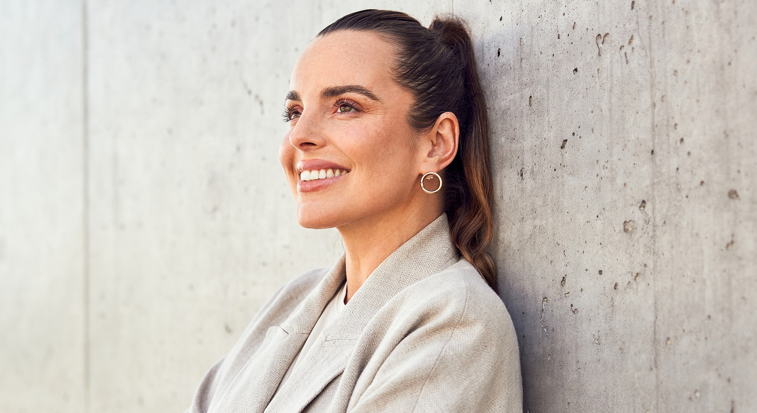 Smiling woman leaning against a concrete wall.